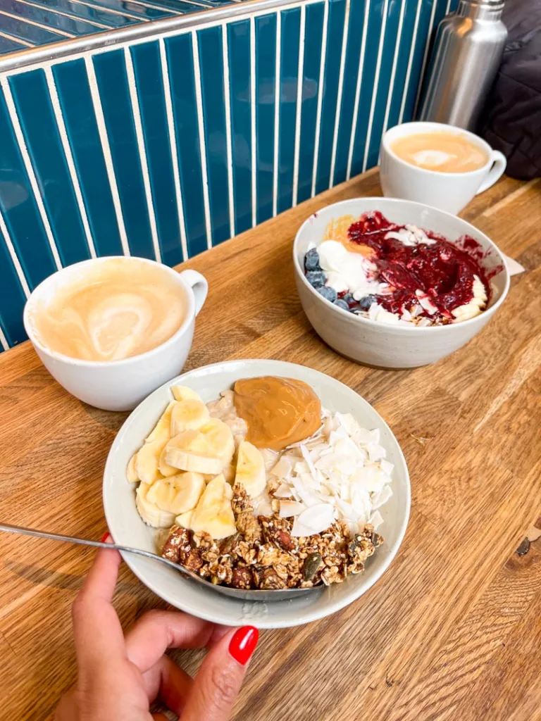 two bowls of porridge topped with banana, coconut flakes and peanut butter, two cappuccinos on the bar at grod in copenhagen