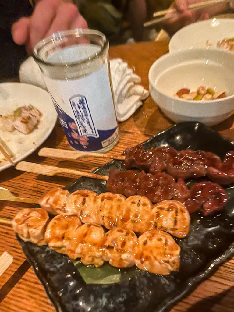 chicken and beef skewers on a table, and a sake cup at buri bar in ebisu, tokyo