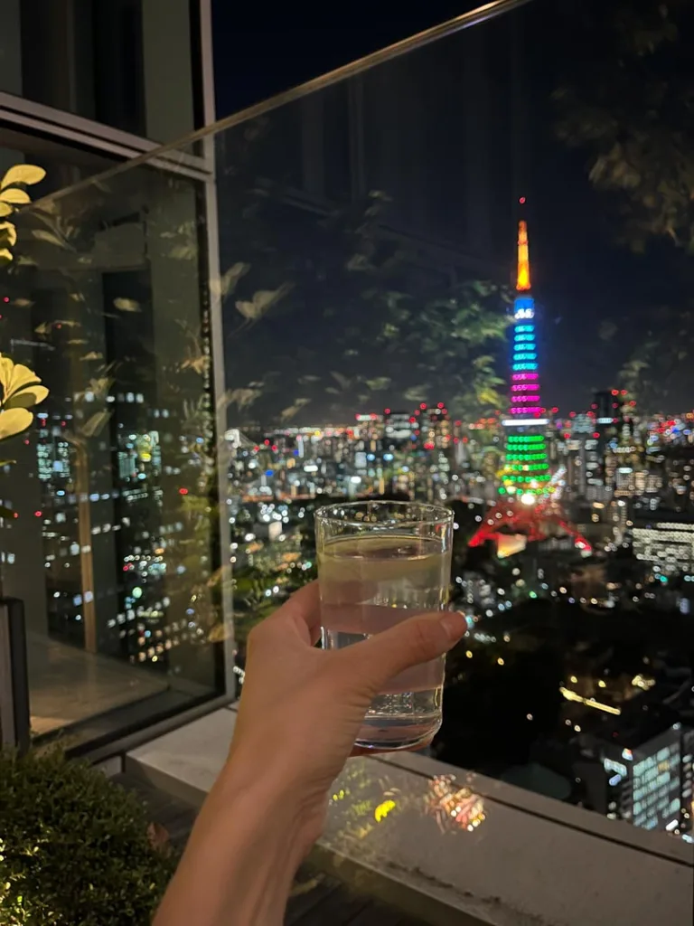 hand holding a drink up the a glass wall with a view of tokyo tower