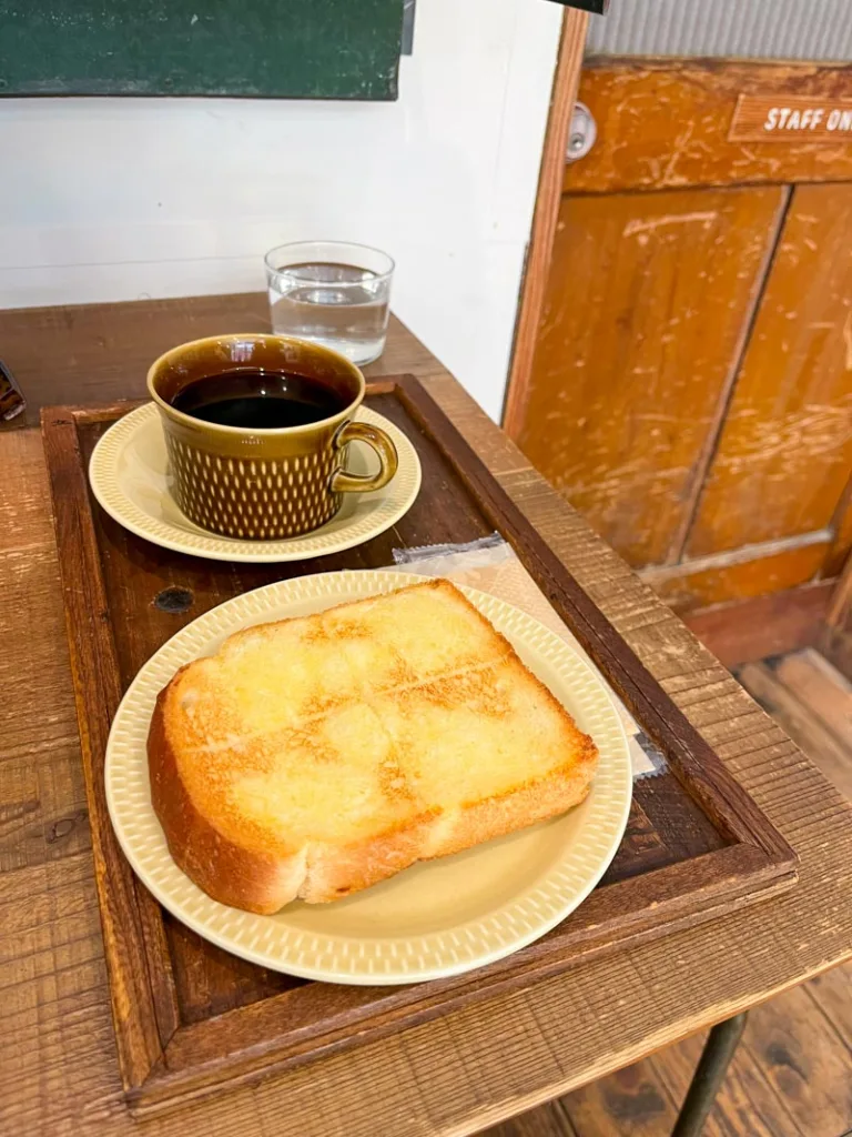 a fluffy slice of buttered toast and a black coffee on a wooden tray at little house coffee shop in tokyo
