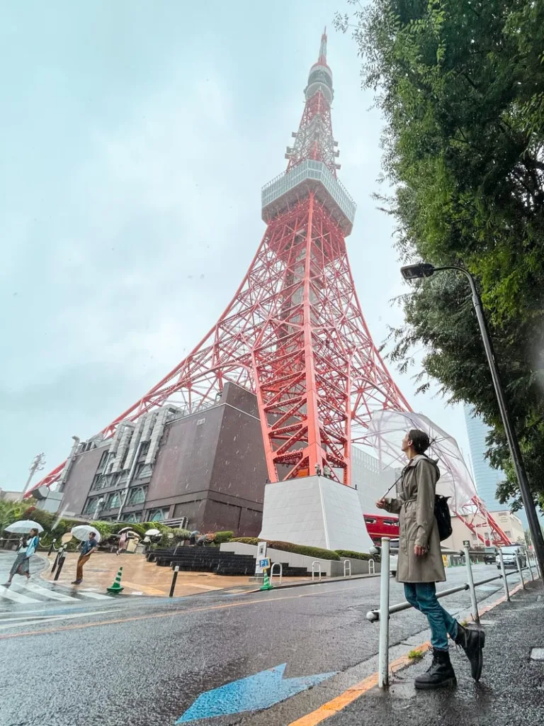 woman standing in front of the red tokyo tower holding an umbrella on a gloomy, rainy day