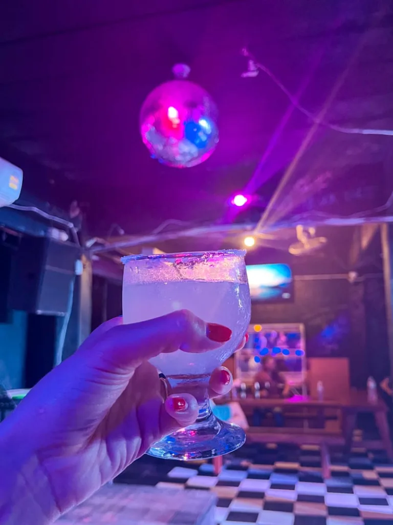 hand holding a margarita, white and black checkered floor and a disco ball hanging on top at a bar in koh tao, thailand