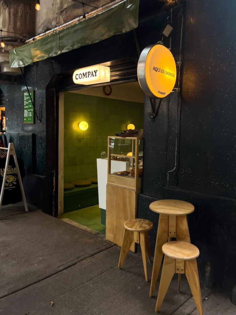 black facade of compay coffee shop, with a small wooden table and two stools outside in mexico city
