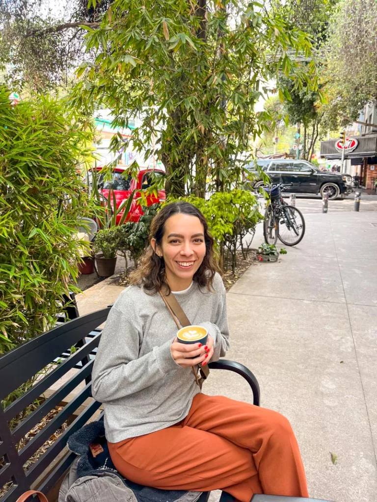 woman sitting on a metal bench having a ceramic mug in her hands outside cucurucho, one of the best coffee shops in mexico city