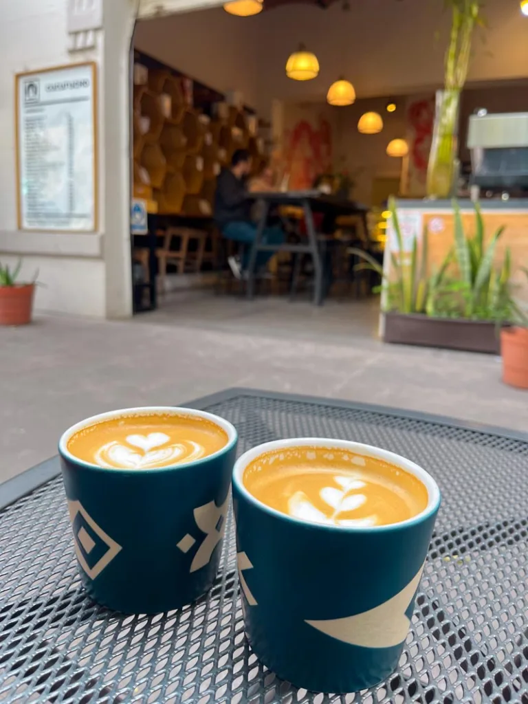 two lattes on a metal table outside cucurucho coffee shop in mexico city