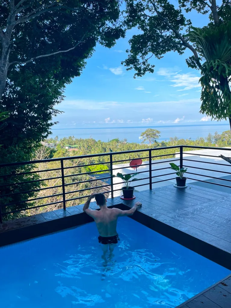 man standing at the edge of a pool on a mountain with a view of the ocean in the distance in koh tao, one of the best islands in thailand