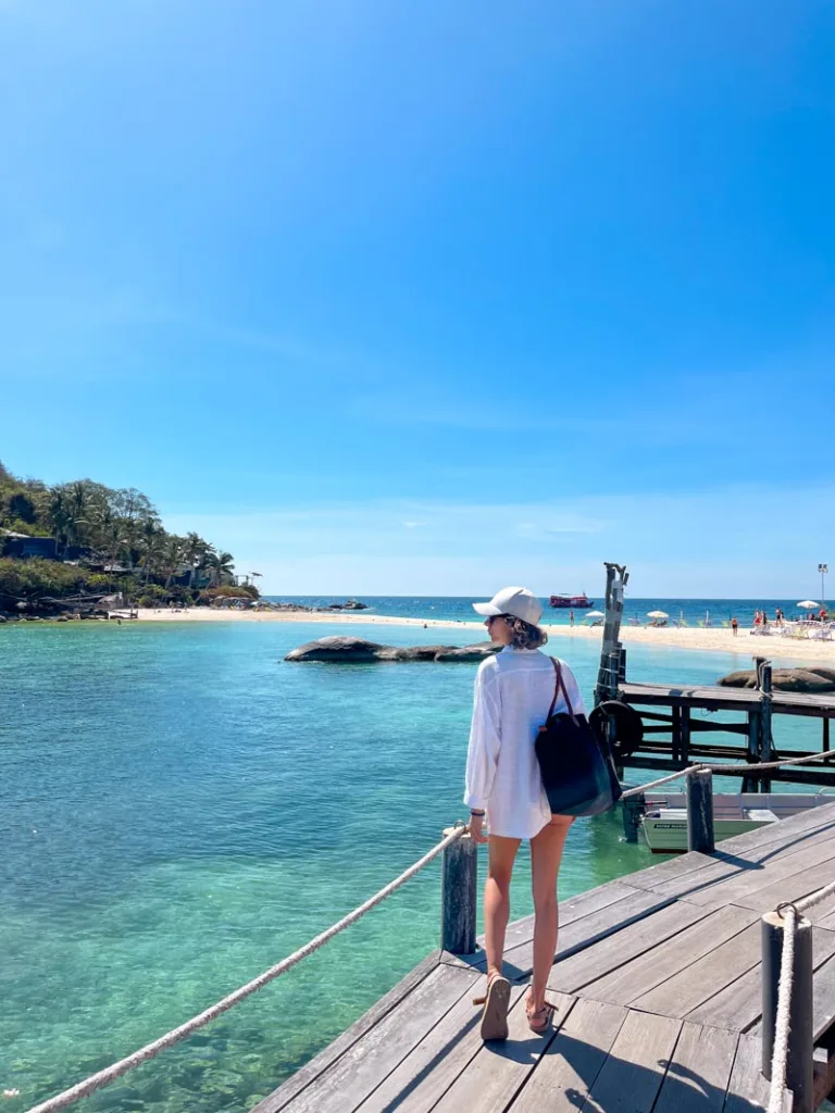 woman standing on a wooden bridge over turquoise water in koh tao, thailand