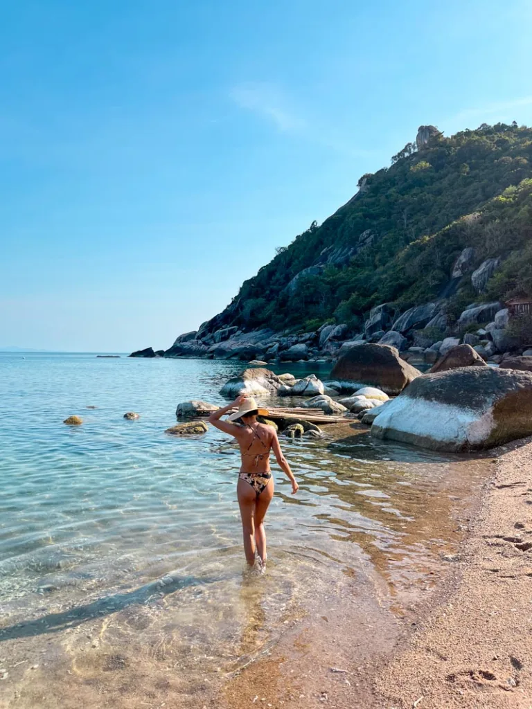 woman in a bikini standing on the beach with her feet in the water in koh tao, thailand