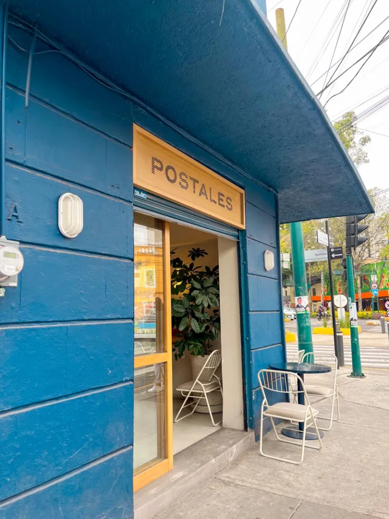 blue facade and a wooden sign with the name of postales coffee shop in mexico city