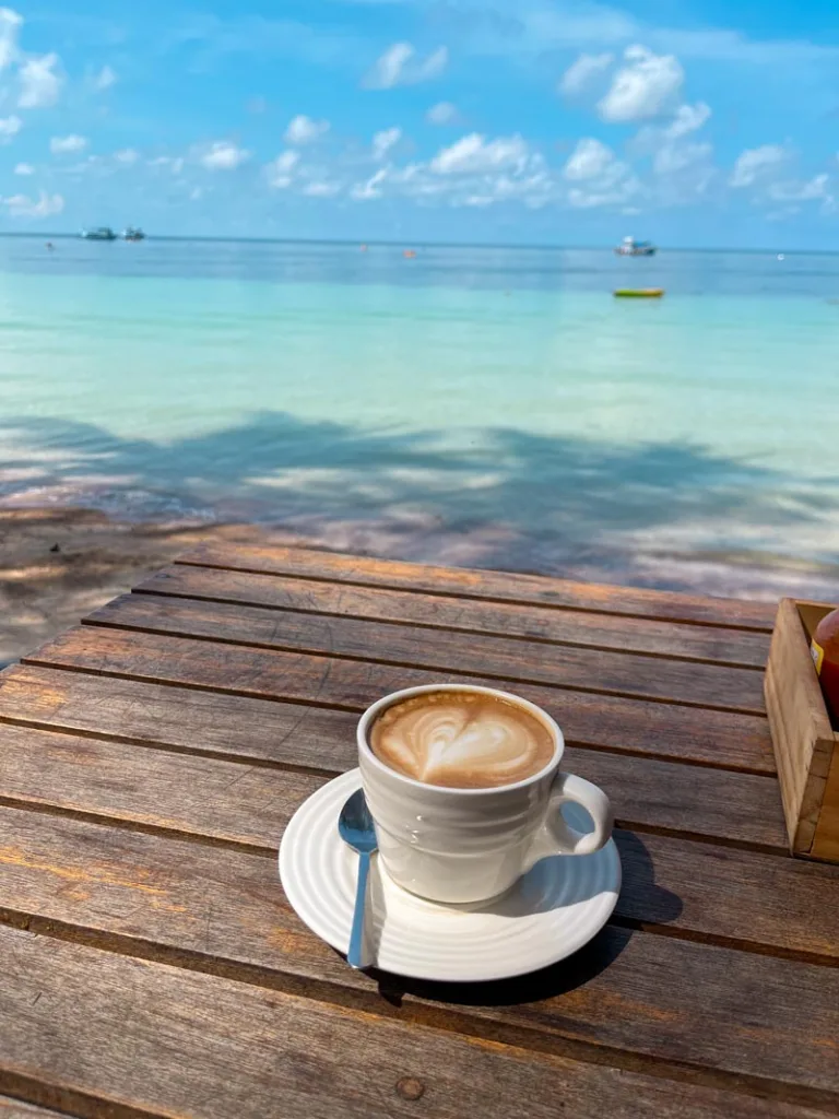 cappuccino on a wooden table in front of the bright turquoise ocean at cafe culture in koh tao, thailand