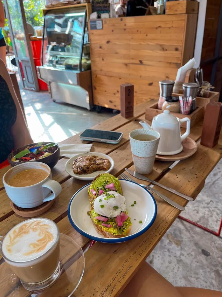 eggs benedict on the table, two coffee cups, a cookie, and an acai bowl at factory cafe, one of the best places to eat in koh tao