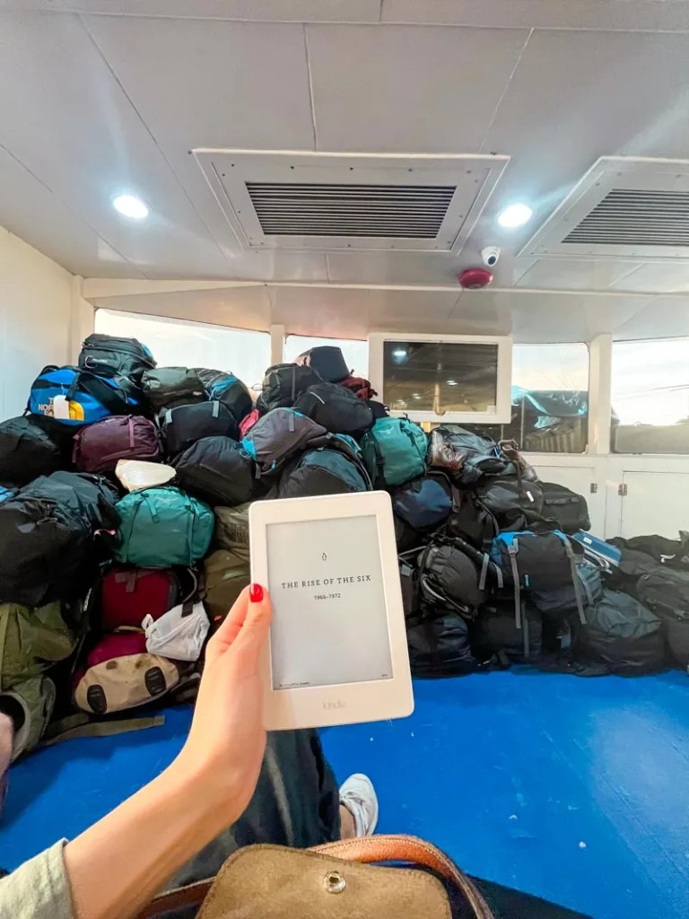 hand holding a kindle with a mountain on luggage at the back on a ferry going to koh tao, thailand