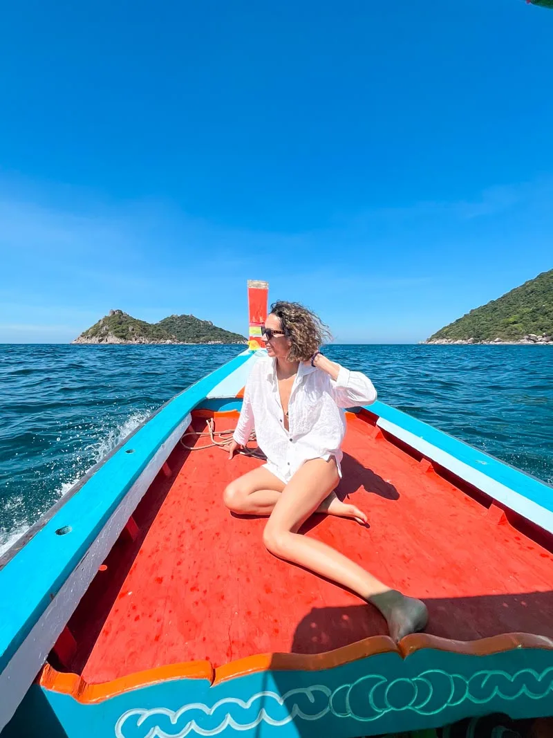 woman sitting on the front base of a thai long tail boat in koh tao, thailand