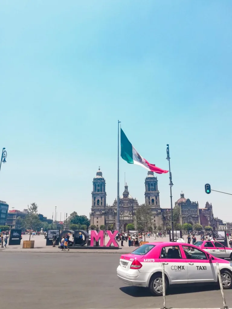 a pink taxi in front of el zocalo in mexico city with a big mexican flag hanging behind