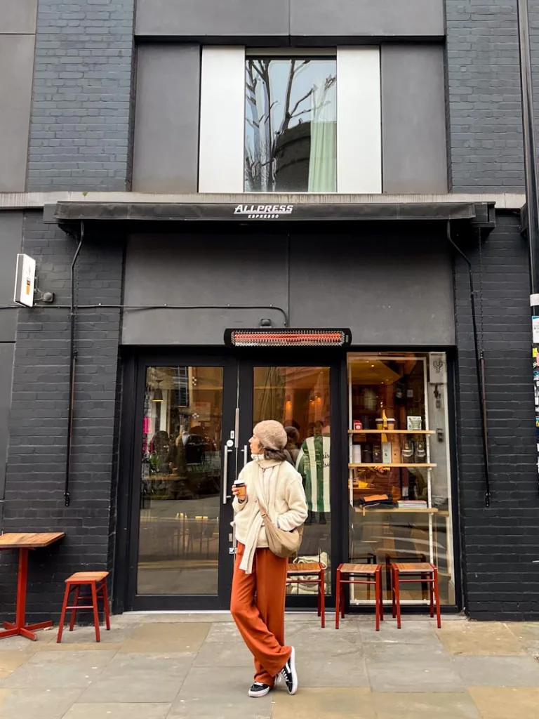 woman standing outside an allpress coffee shop in london holding a takeaway coffee cup