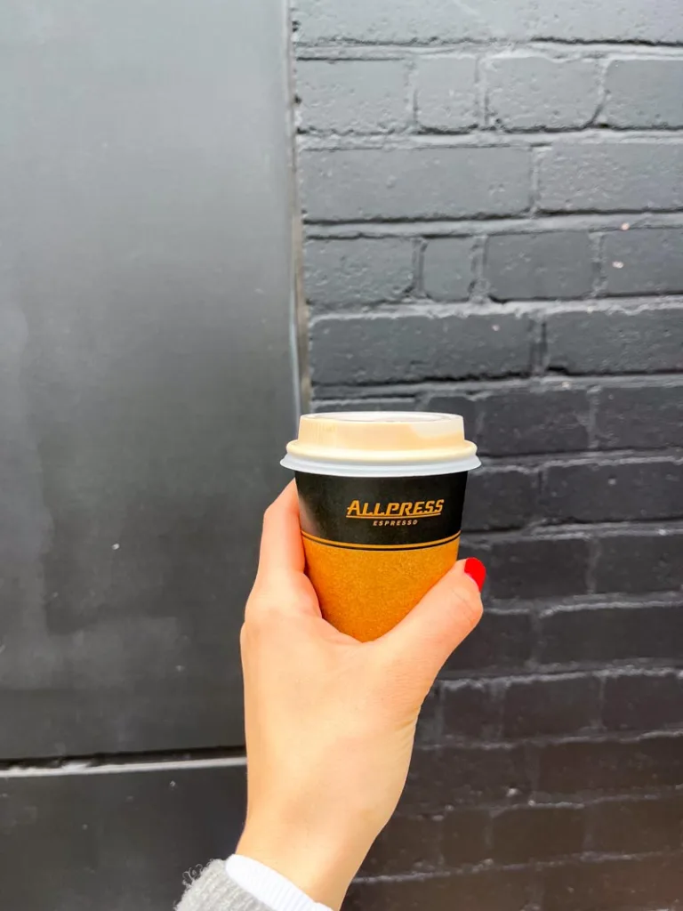 hand holding a take way cup from allpress espresso coffee shop in shoreditch, london