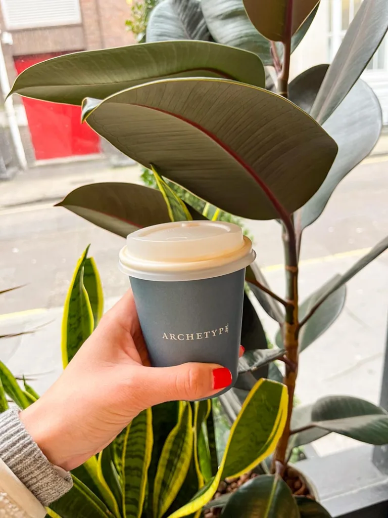 hand holding a take away coffee cup at archetype coffee shop in london