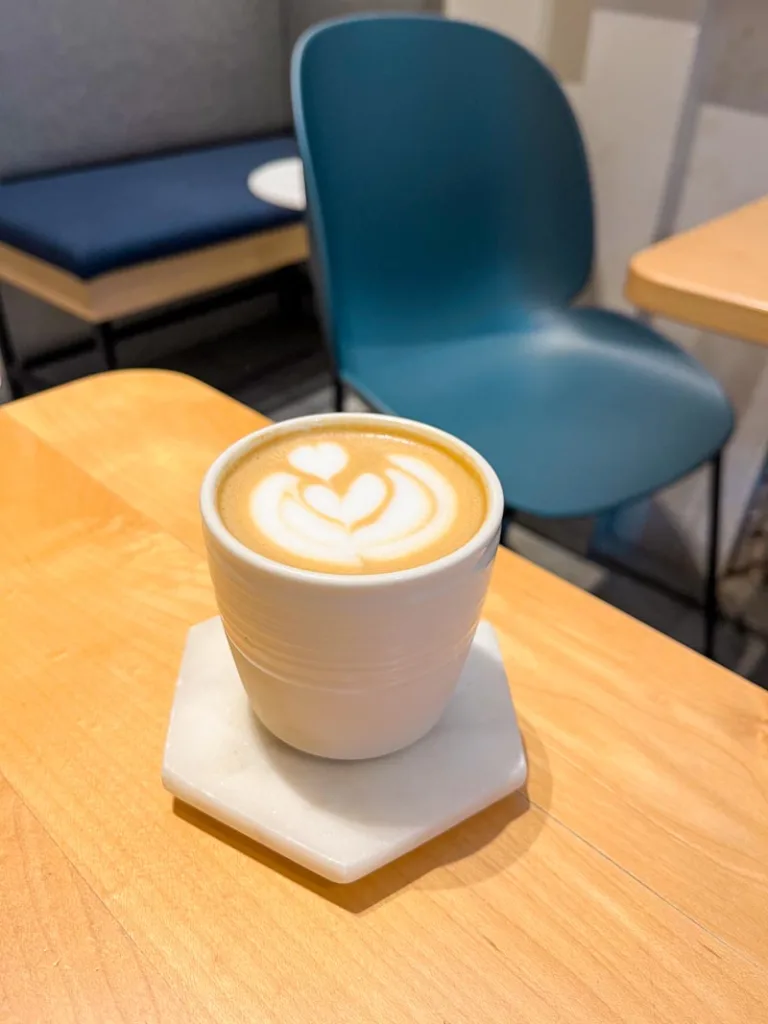 a latte on a white ceramic mug on a wooden table at guillam coffee shop in kensington, london