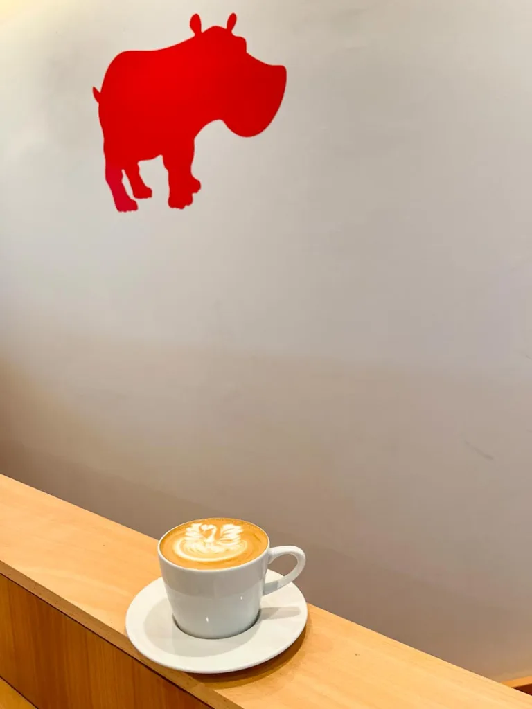 latte on a wooden bar with a red hippo image on the wall at kiss the hippo coffee shop in london