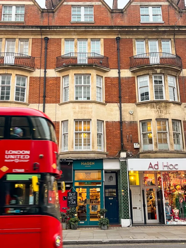 red double decker bus driving in front of a red brick building in london