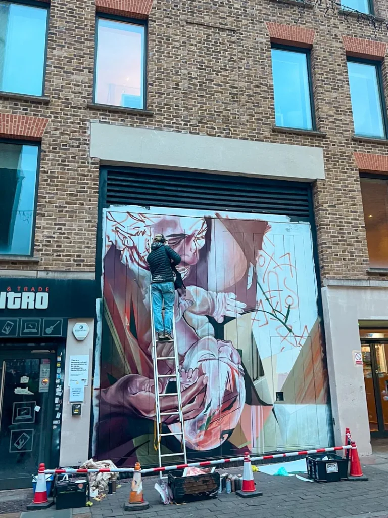 street artist up on a ladder painting a mural in shoreditch, london