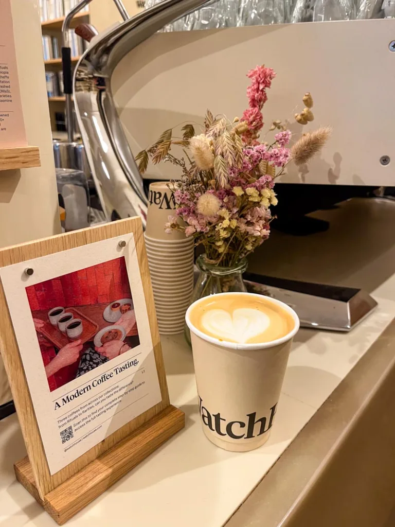 an open takeaway latte on the bar next to a flower vase at watch house coffee shop in london
