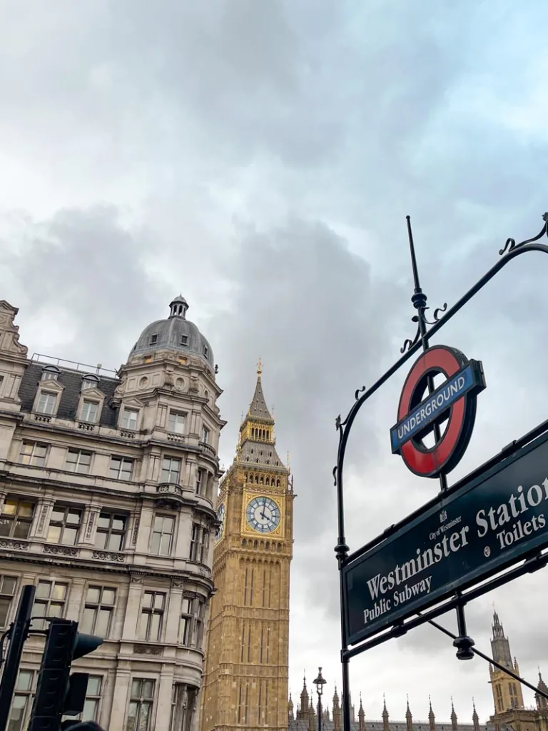 metro entrance sign of westminster station in london with a view of big ben behind