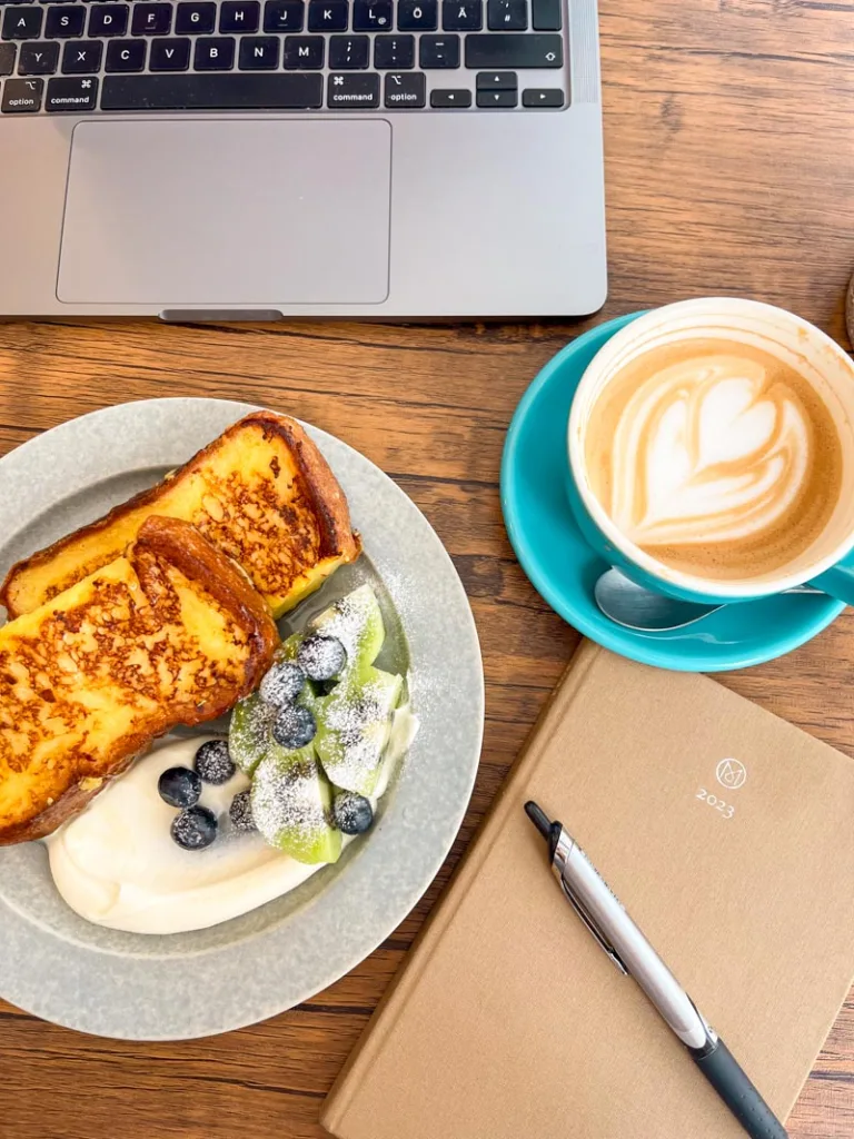 overview of a plate of french toast with whipped cream and berries, a latte, and an agenda with a pen on top at cafe tales in osaka