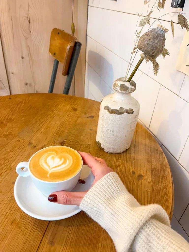 hand holding a white coffee cup on a white saucer plate, on a wooden table, at boot cafe in paris