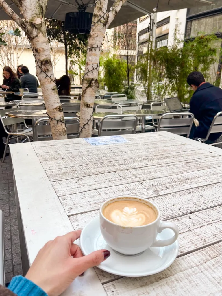 hand holding a coffee cup on an outdoor wooden table at certified cafe in paris