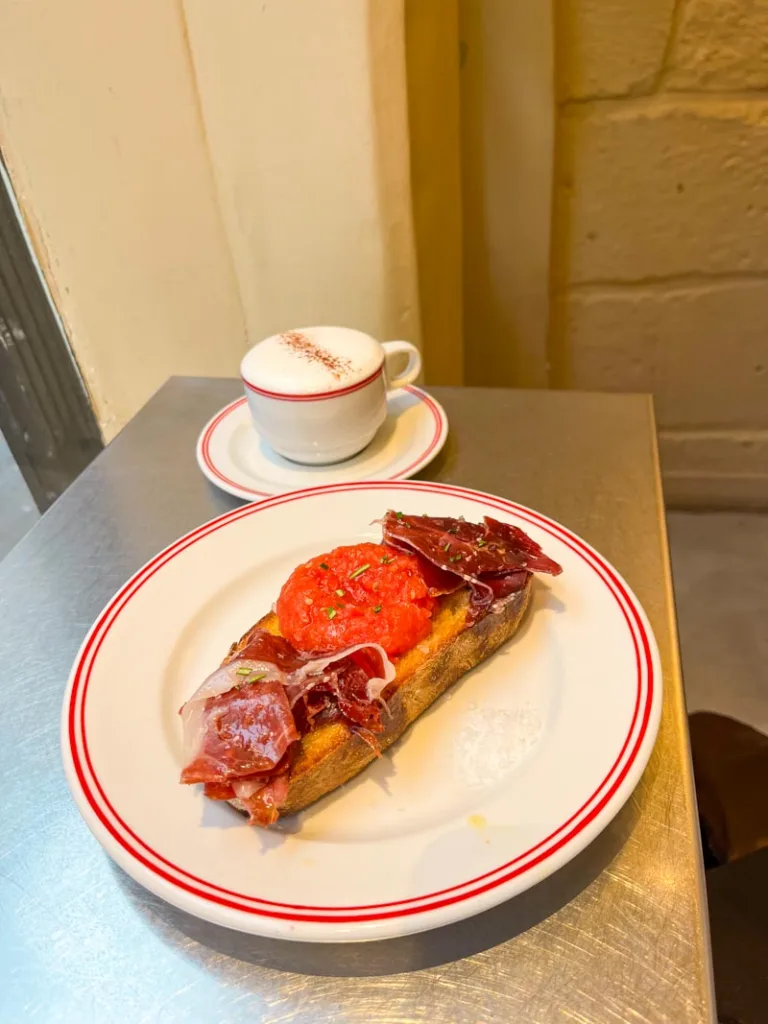 plate with pan con tomate and jamon iberico and a capuccino on the side at cortado coffee shop in paris