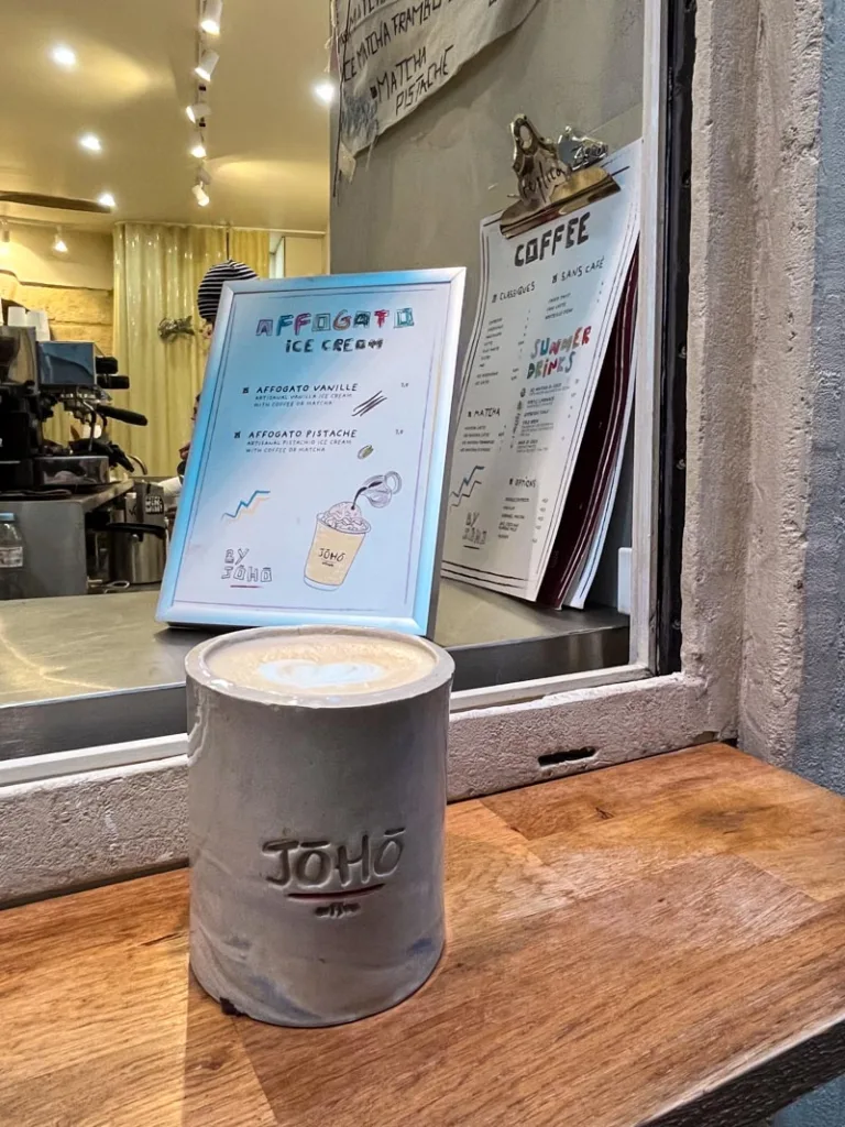 a latte in a ceramic coffee cup with joho carved into it on a wooden bar, with a view of the coffee shop menu behind