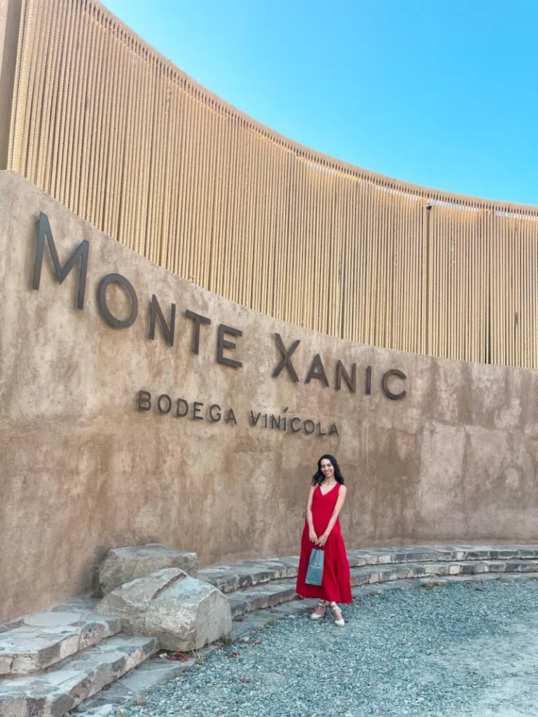 Woman in a red dress standing in front of the entrance sign of Monte Xanic winery in Valle de guadalupe