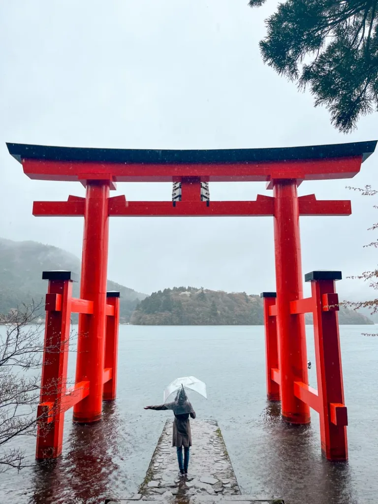 Woman standing under the massive torii gate emerging from the lake at Hakone Shrine
