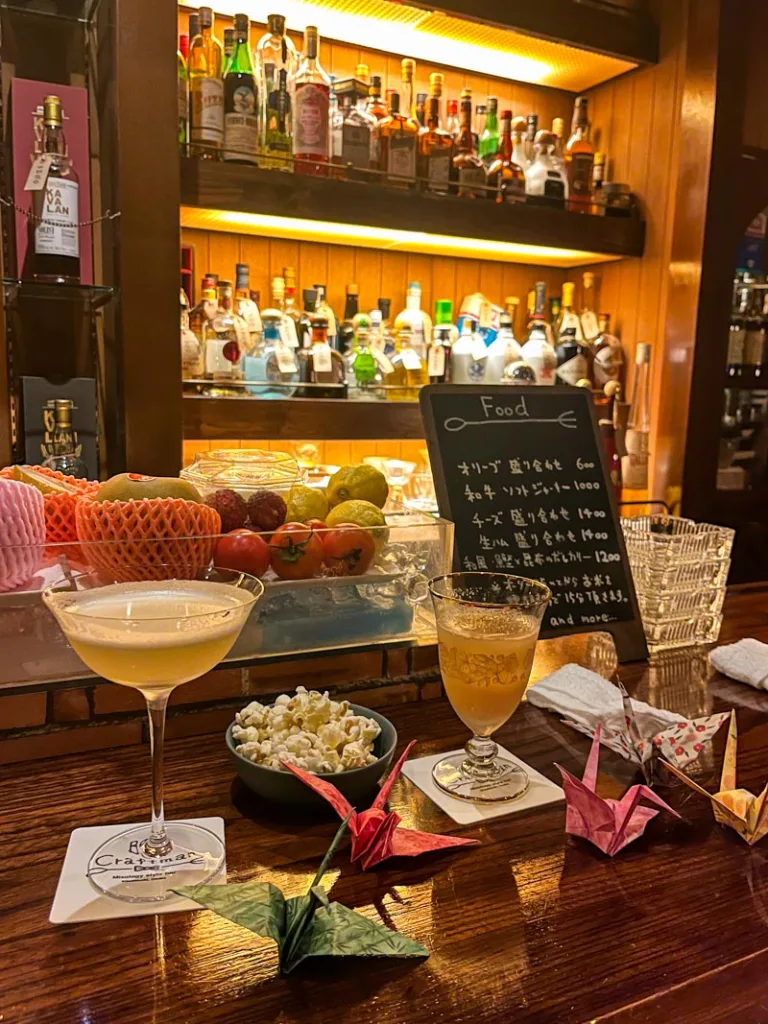 Cocktails, a popcorn bowl and paper cranes on a wooden bar at Bar Craftman in Osaka