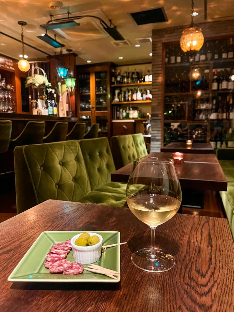 Wine glass and a small plate with salami and olives at Bar Francais Le chat noir in Osaka