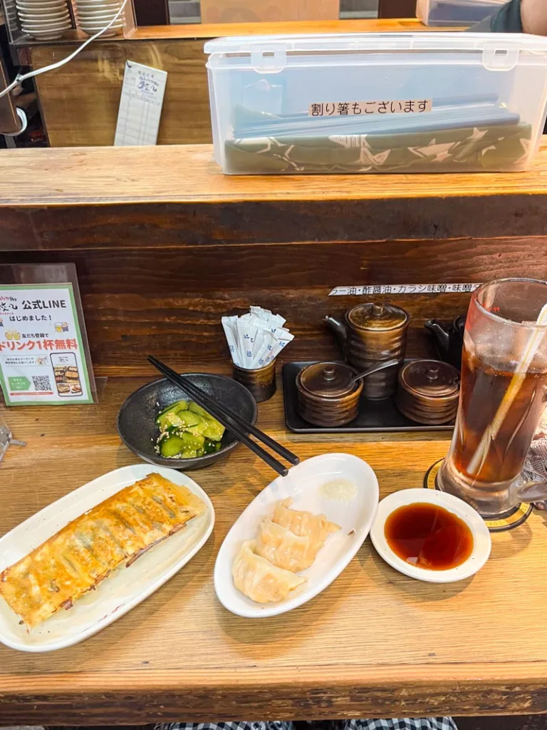 Plates of gyozas, spicy cucumber, and a soda on the wooden bar at chao chao gyoza in osaka, one of the best cheap eats