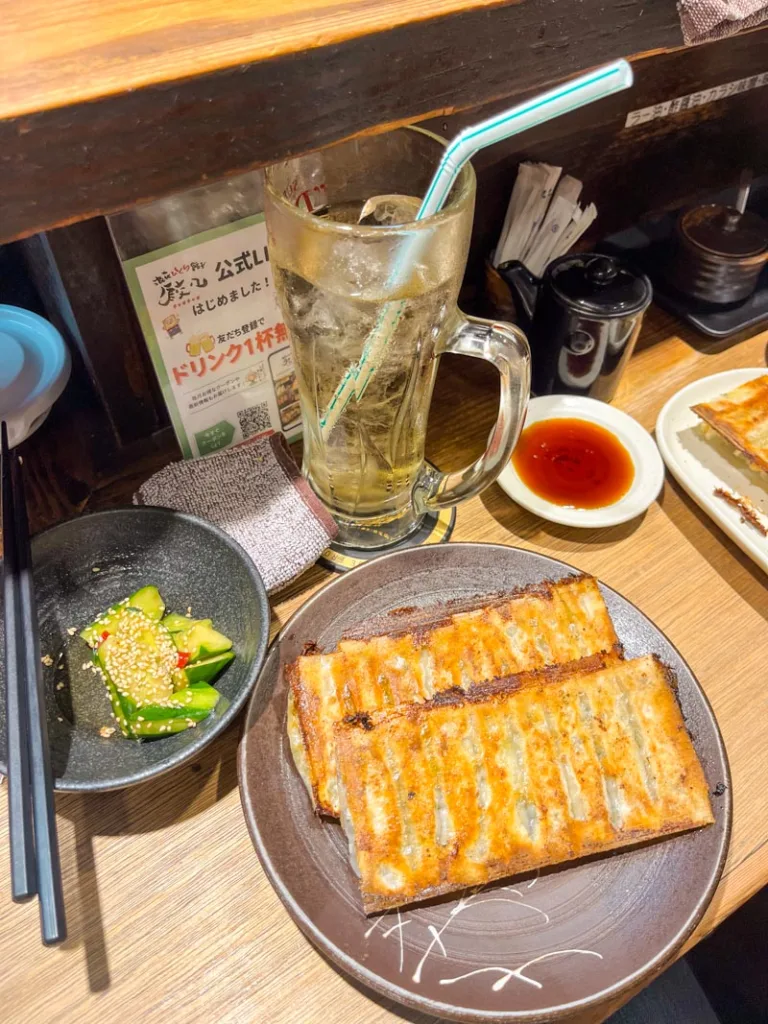 Plate of gyozas, spicy cucumber, and a high ball on the wooden bar at chao chao gyoza in osaka, one of the best cheap eats