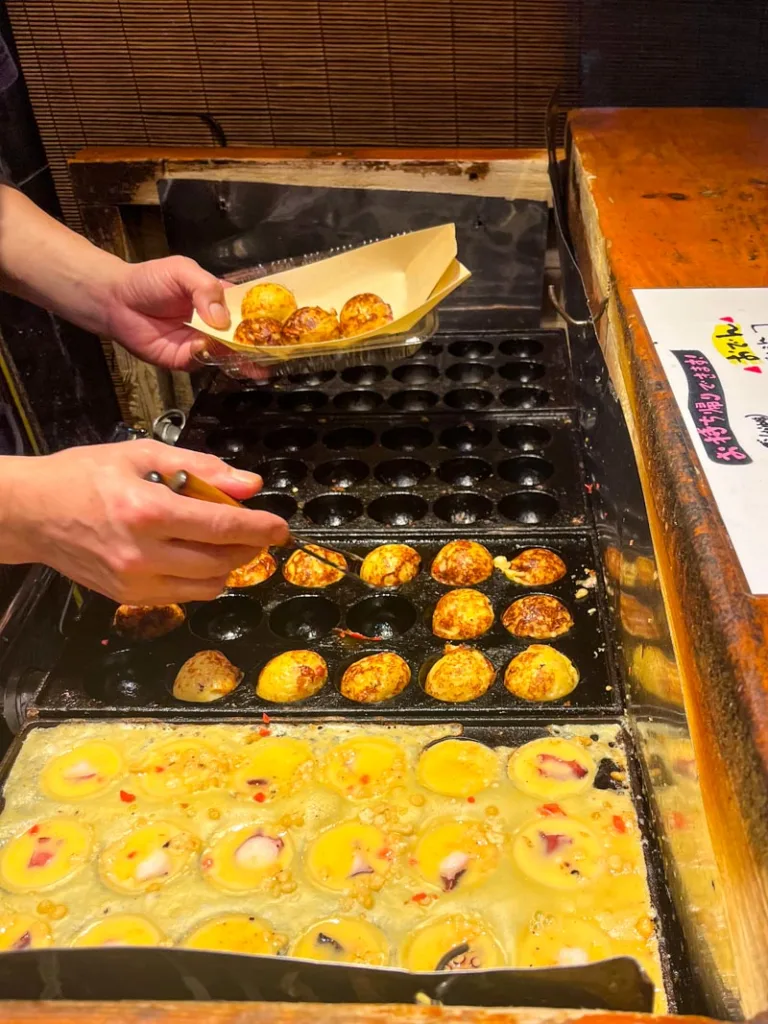Man making takoyaki on a takoyaki pan at hiyoko, one of the best cheap eats in Osaka