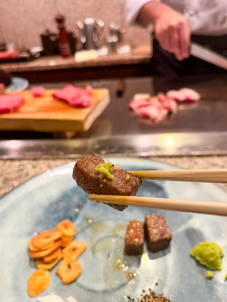 Chopsticks holding a piece of cooked kobe beef with wasabi