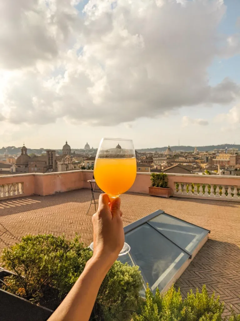 Hand holding a spritz at Terrazza Caffarelli in Rome with a view of the citys rooftops