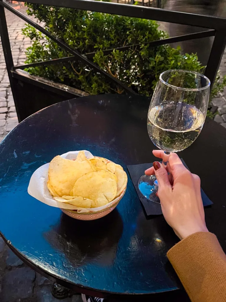 Hand holding a wine glass on a table with a bowl of chips at Big Hilda Public Bar in Trastevere