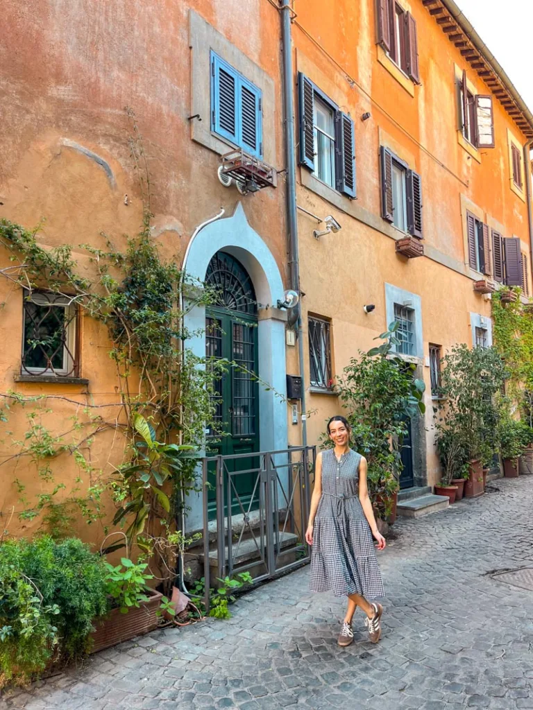 Woman standing in front of a orange house lined with plants