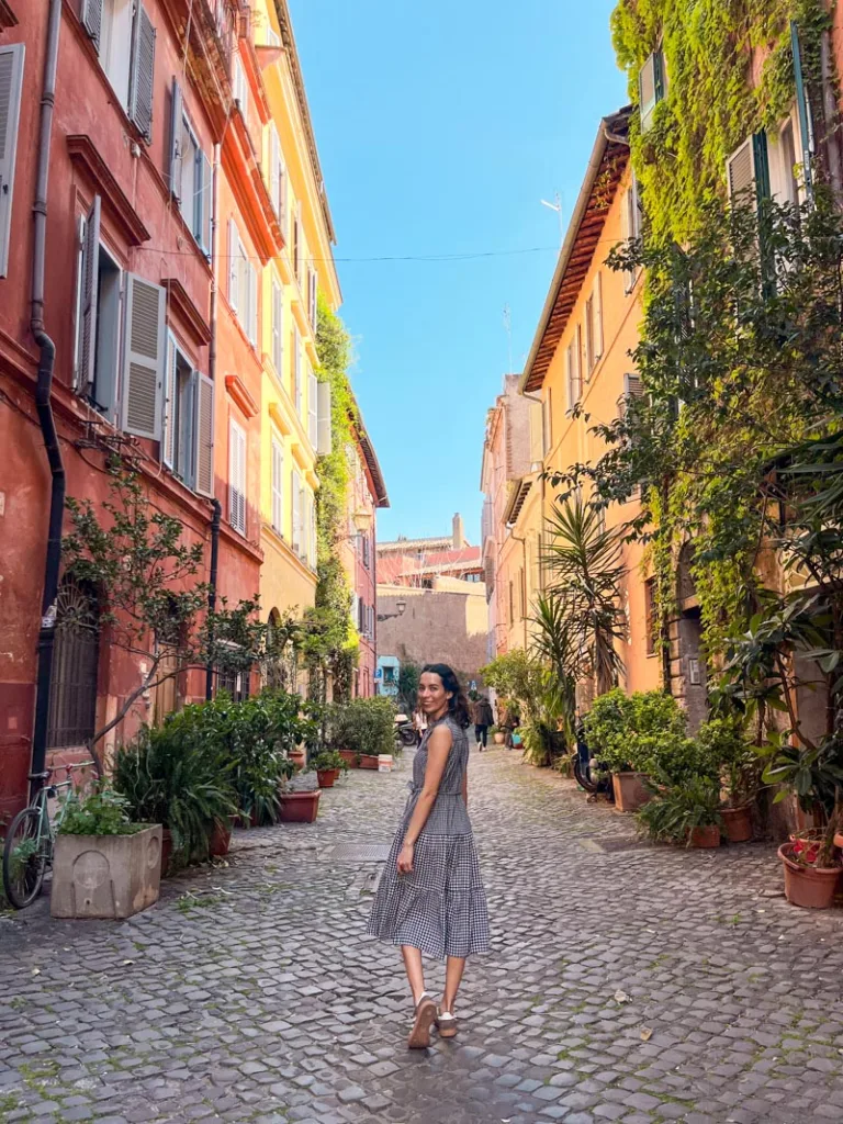 Woman walking along a colorful cobblestone street surrounded by plants and pastel buildings in Trastevere.