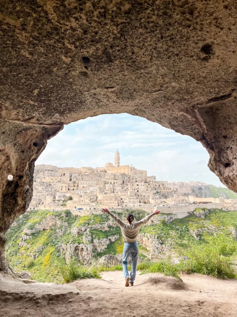 Woman standing inside a cave with a view of Matera in the distance
