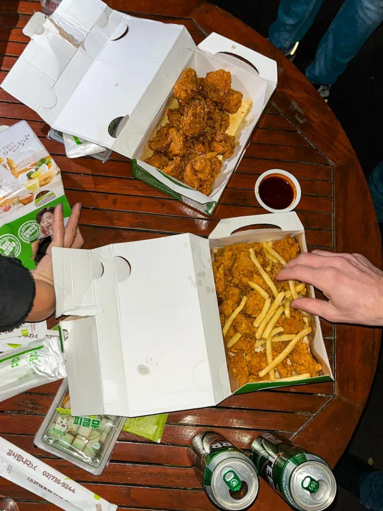 hands digging into boxes of korean fried chicken on a wooden table