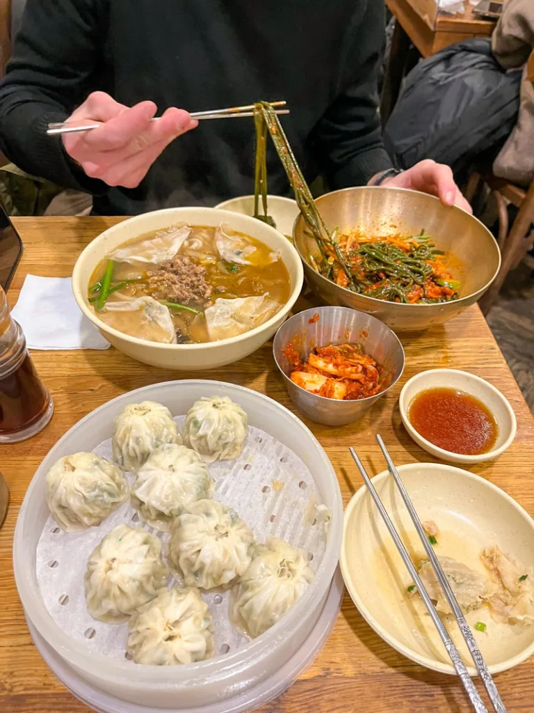 a plate of dumplings, a side of kimchi, and a bowl of dumpling soup at myeongdong kyoja restaurant in seoul