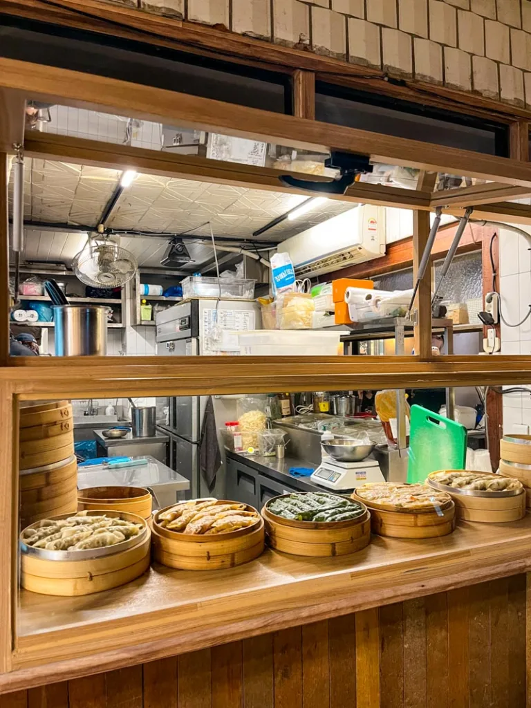 a window overlooking the kitchen of a dumpling restaurant, with a few dumpling steamer baskets on display with various dumplings in ikseondong seoul