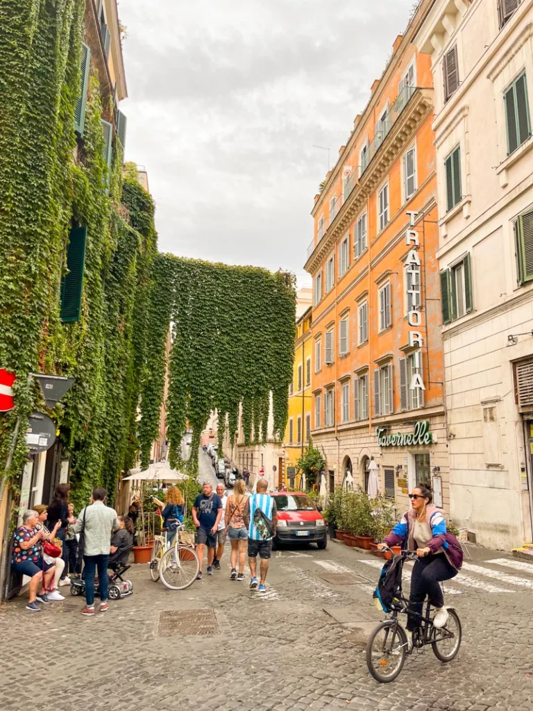 Locals and tourists enjoying a sunny day at a cobblestone street café in Monti, Rome.