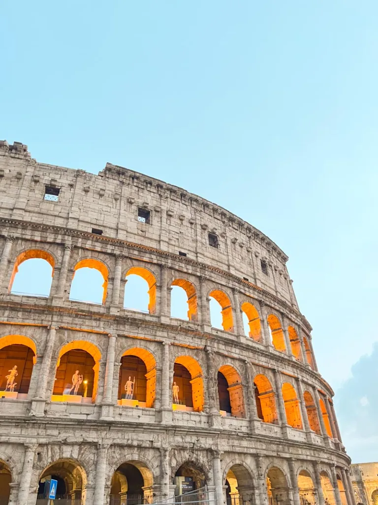 The Colosseum in Rome glowing at sunset with a soft blue sky overhead, in Centro Storico, one of the best places to stay in Rome for first timers